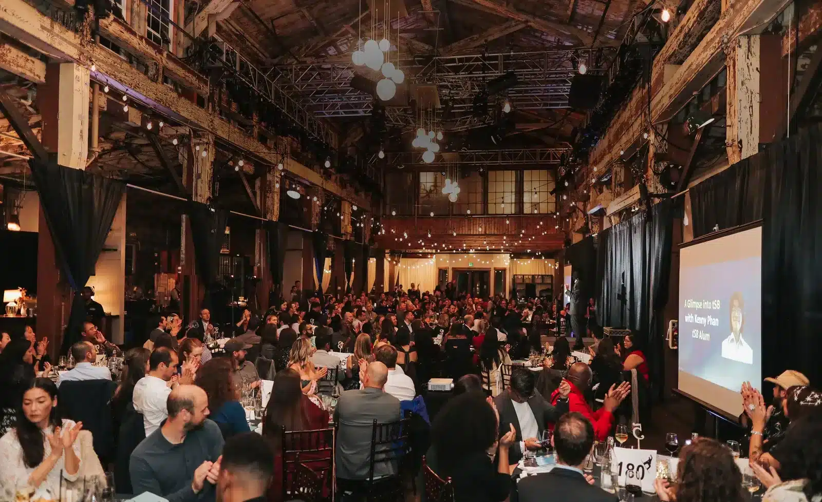 A packed company dinner in the SoDo Park hall, with hundreds of guests beneath the timber trusses and a presentation on screen, Seattle