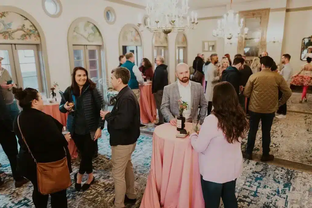 Colleagues networking around cocktail tables beneath crystal chandeliers at The Ruins, a corporate event venue in Seattle