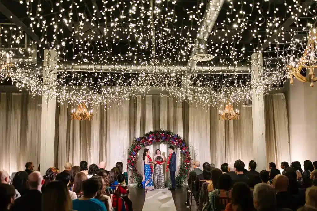 A Hindu wedding ceremony beneath a rose and orchid arch and a ceiling of twinkling lights at Hideaway Cellars, with family seated on both sides