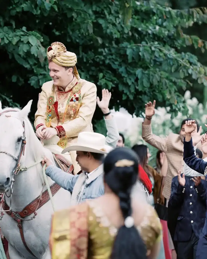A groom arriving on a white horse for his baraat, surrounded by dancing family at Fox Hollow Farm