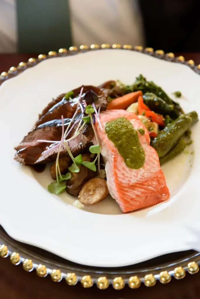 A plated Herban Feast entrée of salmon and beef with seasonal vegetables on gold-rimmed china