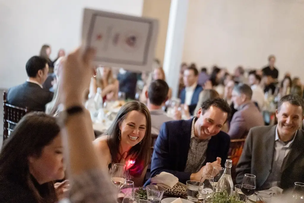 Gala guests laughing at their table as bid cards go up during a fundraiser auction