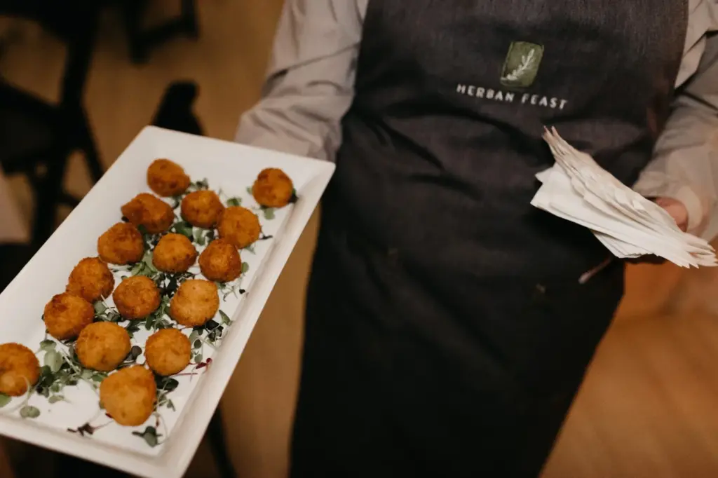 A Herban Feast server passing a tray of hot appetizers at an evening gala