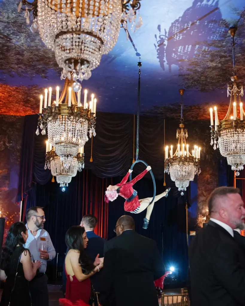 An aerialist performing beneath crystal chandeliers in the ballroom at The Ruins during an evening event