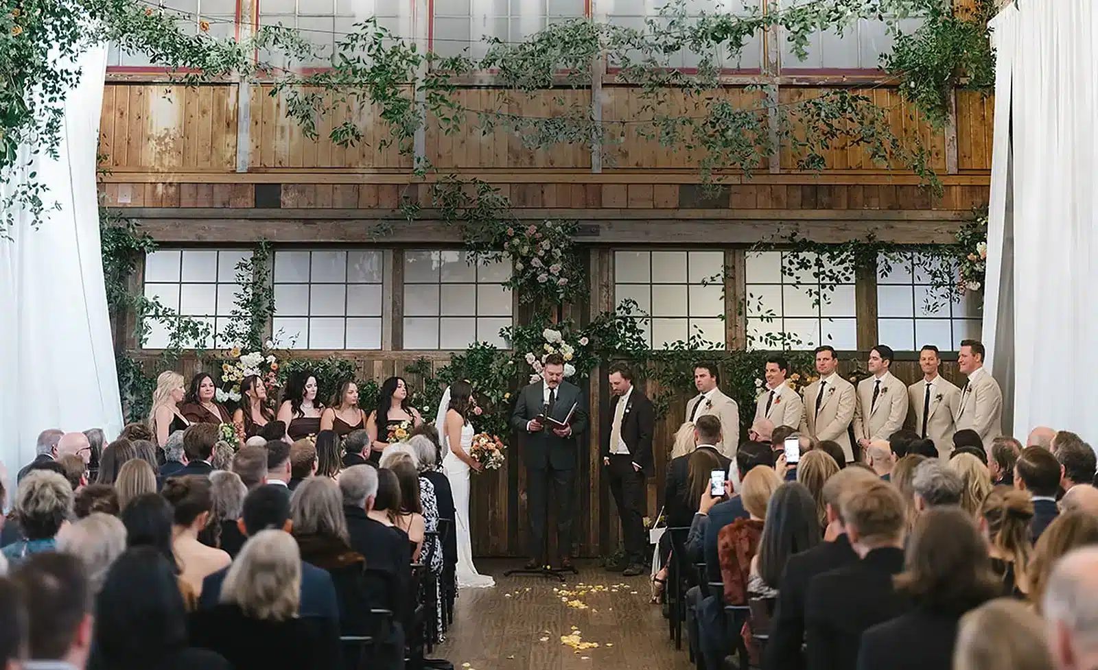 A packed wedding ceremony beneath a greenery-draped wall at SoDo Park, a large wedding venue in Seattle