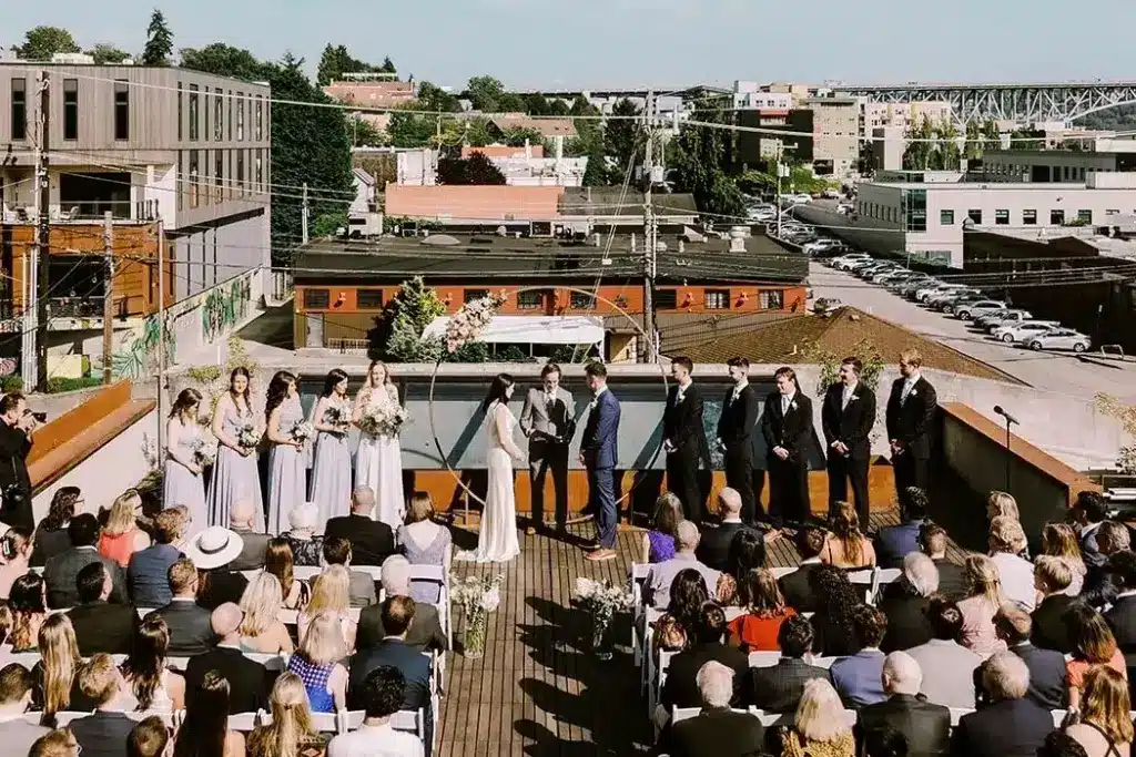 A large rooftop wedding ceremony at Fremont Foundry, with the full wedding party and rows of guests above Fremont, Seattle
