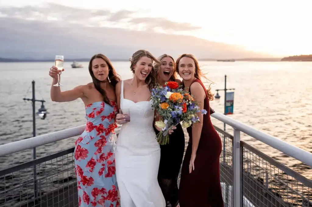 A bride and bridesmaids celebrating on the balcony over Elliott Bay at The Point at Pier 70, a waterfront wedding venue in Seattle
