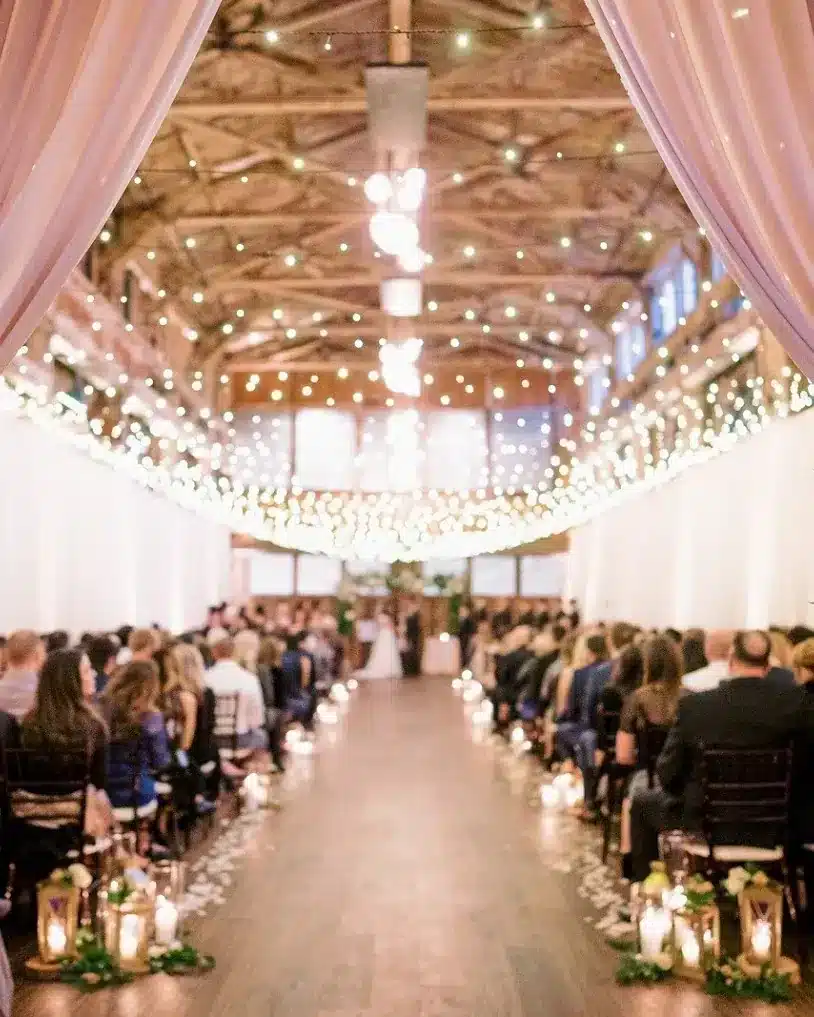 A candlelit aisle framed by blush drapery with a full hall of guests at SoDo Park, a large wedding venue in Seattle