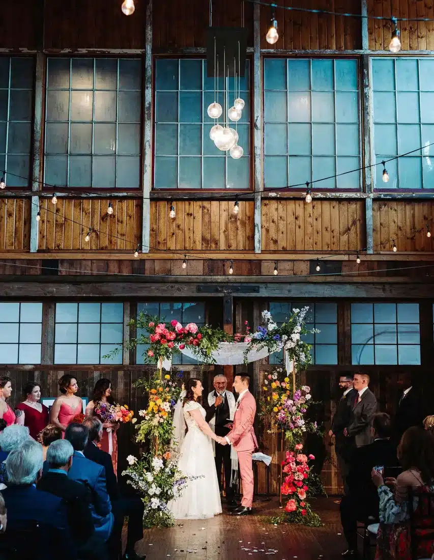 A ceremony at Fremont Foundry with string lights, pendant lighting and a floral arch