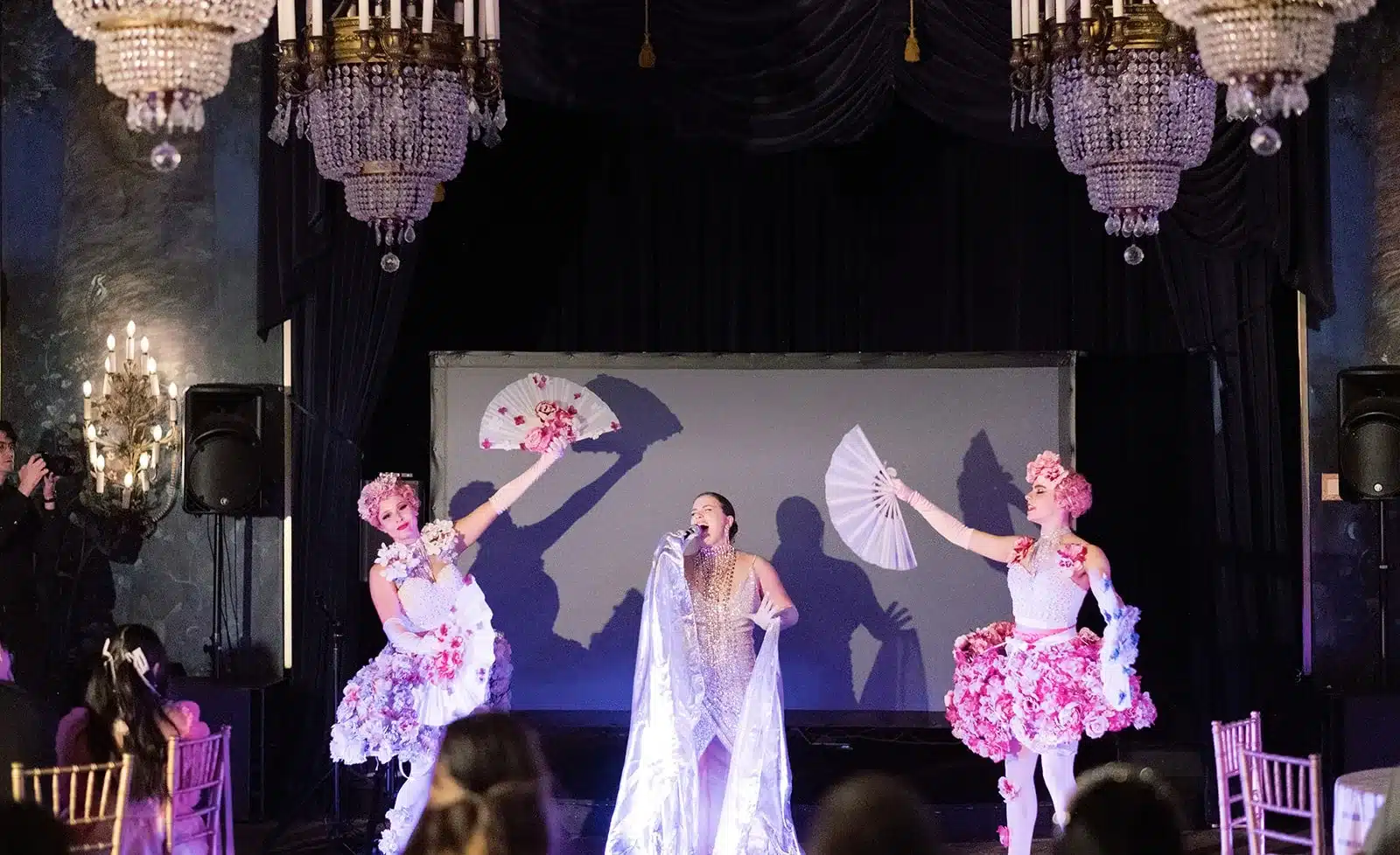Performers on stage beneath crystal chandeliers at a milestone birthday party in The Ruins ballroom, Seattle