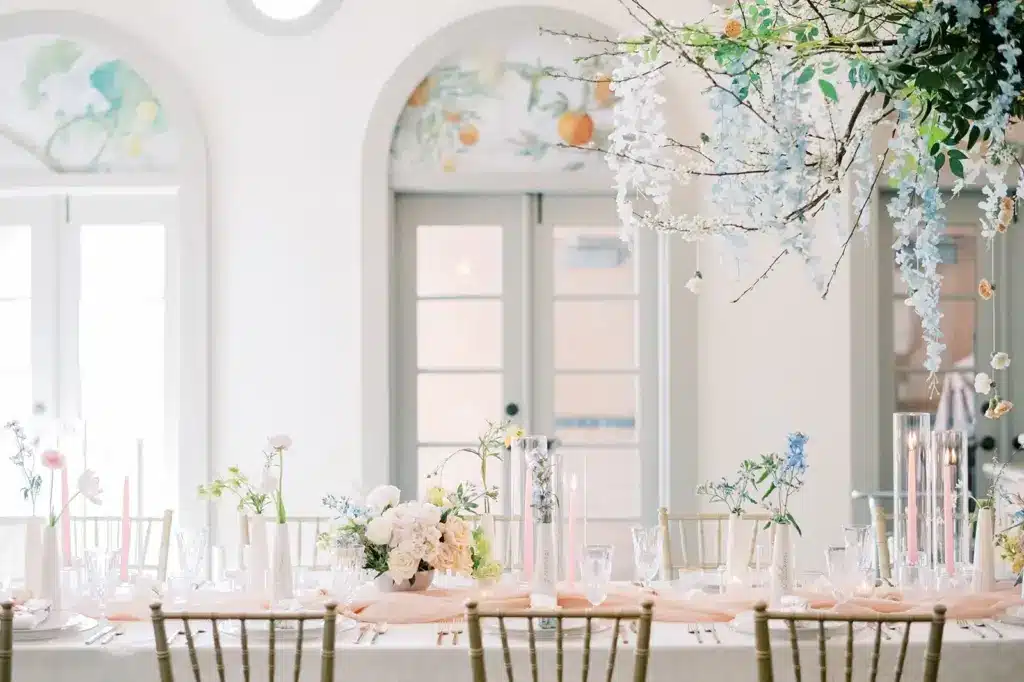 A birthday dinner table set with blush linens, taper candles and spring flowers beneath arched windows