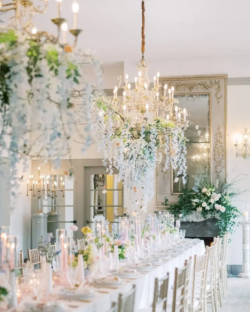 A long birthday dinner table under crystal chandeliers and hanging florals at The Ruins